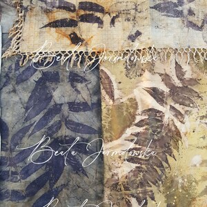 May include: A close-up of two fabric squares with a leaf pattern. The fabric is a light beige color with brown and black leaf patterns. The fabric is textured and has a fringe border. The name "Beata Jarmolowska" is written in white cursive on the fabric.