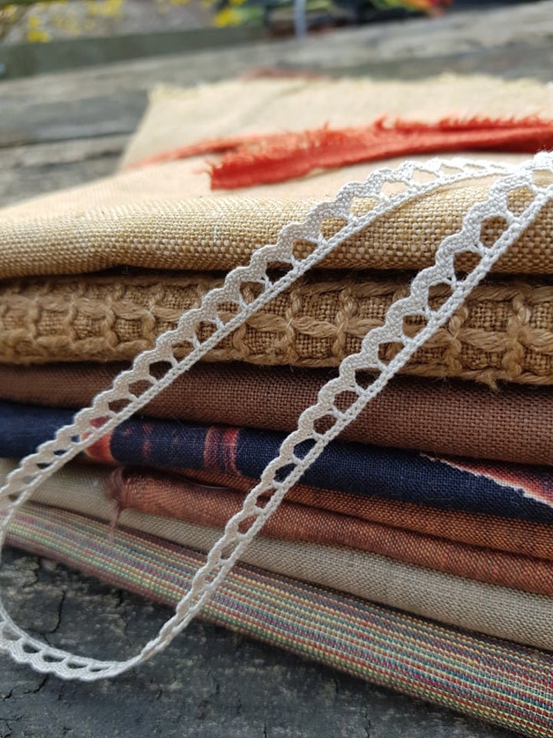 Puede incluir: Una pila de muestras de tela en varios colores y texturas, incluyendo marr&oacute;n, beige y azul, con un ribete de encaje blanco tejido a crochet.
