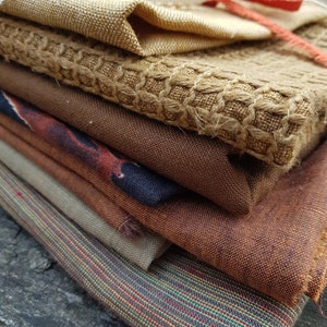 Puede incluir: Una pila de muestras de tela en varios tonos de marr&oacute;n, beige y naranja. Las telas tienen diferentes texturas, incluyendo tejidas, de punto y texturizadas.
