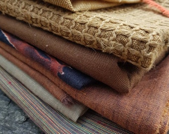 May include: A stack of fabric swatches in various shades of brown, beige, and orange. The fabrics have different textures, including woven, knitted, and textured.