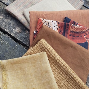 Puede incluir: Un conjunto de seis muestras de tela en varios tonos de marr&oacute;n, beige y tostado. Las telas tienen diferentes texturas, incluyendo un patr&oacute;n tejido, un lino liso y una tela estampada con puntos negros y blancos.