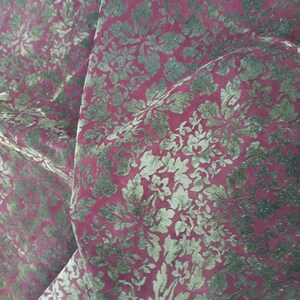 May include: Close-up of a red fabric with a gold floral pattern. The fabric has a textured, velvety feel.