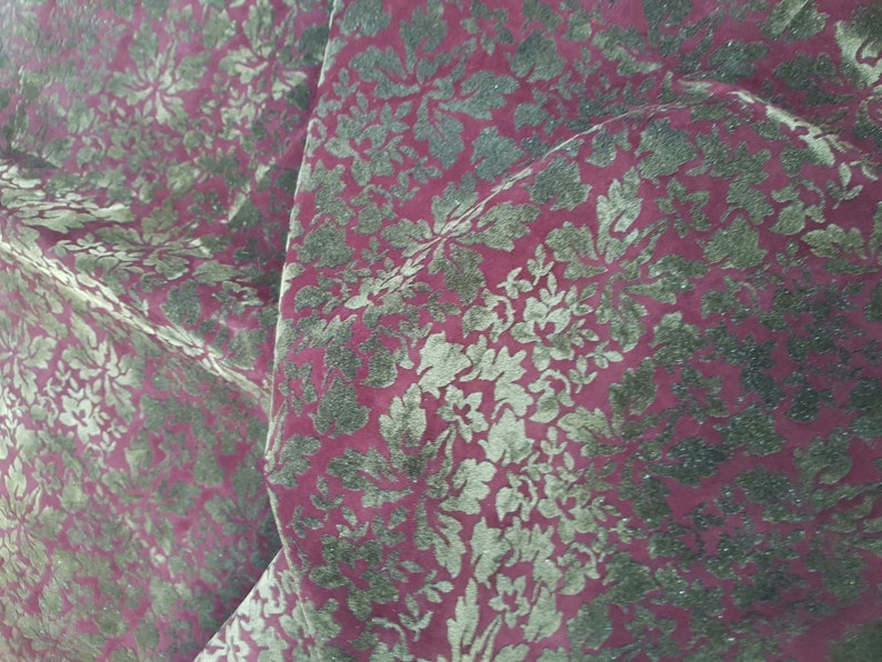 May include: Close-up of a red fabric with a gold floral pattern. The fabric has a textured, velvety feel.