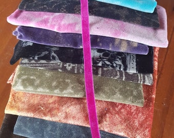 May include: A stack of fabric swatches in various colors and textures, including black, blue, green, orange, and purple. A pink velvet ribbon runs vertically down the center of the stack.