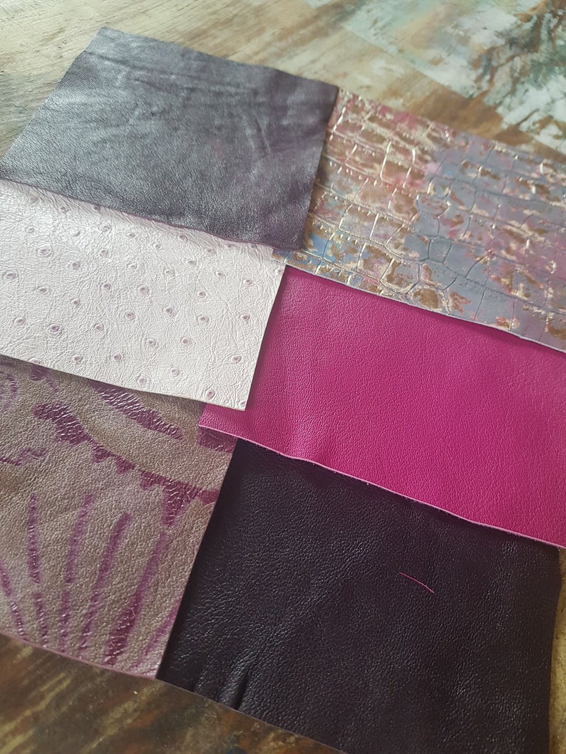 May include: Six different swatches of leather in various colors and textures, including a dark gray, a light pink with a textured pattern, a bright pink, a dark purple with a floral pattern, a dark gray with a textured pattern, and a light gray with a crocodile pattern.