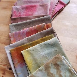 Puede incluir: Una pila de diez cuadrados de tela en varios tonos de marrón, amarillo, naranja y rosa. Los cuadrados de tela están doblados y dispuestos en un patrón de degradado, con los colores más claros en la parte superior y los colores más oscuros en la parte inferior.