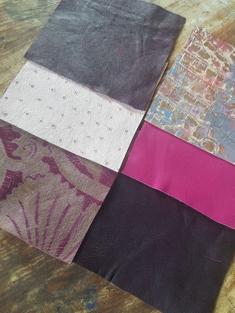 May include: Six different swatches of leather in various colors and textures. The swatches include a dark purple, a light pink with a dotted pattern, a dark purple with a floral pattern, a bright pink, a dark gray, and a light gray with a crocodile pattern.