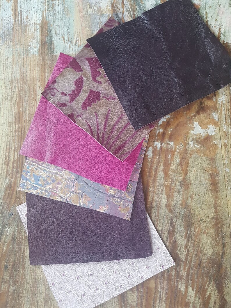 May include: A collection of six different fabric swatches in various shades of purple and pink. The swatches are arranged in a fan shape, with the darkest purple swatch at the top and the lightest pink swatch at the bottom.