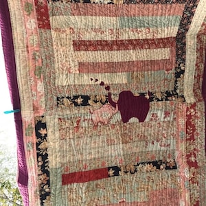 May include: A quilt with a patchwork design featuring floral patterns in shades of pink, red, and brown. The quilt is quilted with a wavy pattern and has a burgundy border.