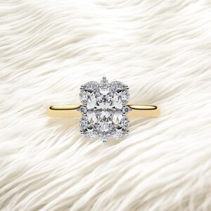 Puede incluir: Un anillo de oro con una gran piedra central de diamante de talla ovalada, rodeada de diamantes más pequeños. El anillo está engastado sobre un fondo blanco texturizado, creando una estética lujosa.