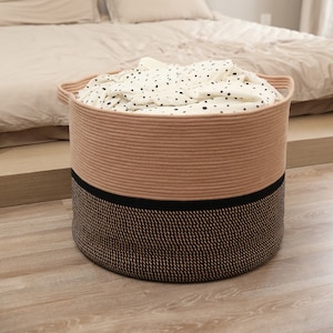 May include: A round, two-toned storage basket with a woven design. The top section is a light brown, the bottom is black, and a black band separates the two. The basket is filled with white fabric with black polka dots. Handles are visible on the sides.