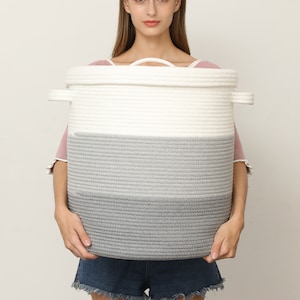 May include: A large, round storage basket with a two-tone design. The top section is white, transitioning to a gray bottom. It has two side handles and a top handle. The basket is made of a thick, woven rope material.