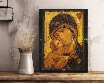 May include: A rectangular religious icon featuring a weathered, golden-toned painting of a figure holding a child, encased in a dark, distressed wooden frame secured with four brass-colored metal studs at the center of each side edge.