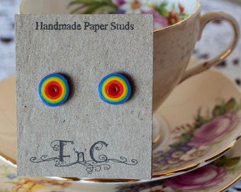 Op de afbeelding: Handgemaakte papieren oorbelletjes met een regenboogontwerp. De oorbelletjes worden getoond op een kaart met de tekst "Handmade Paper Studs" en "FinC".