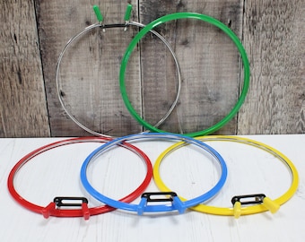 May include: Five embroidery hoops in different colors: red, blue, yellow, green, and silver. The hoops are all the same size and have a simple design.