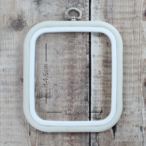 May include: A white embroidery hoop with a silver ring on top. The hoop measures 12.5cm by 14.5cm.