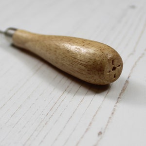 Pu&ograve; includere: Uno strumento in legno con un manico e una punta di metallo. Il manico &egrave; marrone e ha un piccolo foro all'estremit&agrave;.