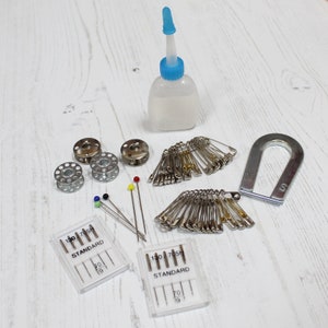 May include: A set of sewing supplies including two packs of needles, two spools of thread, a bottle of sewing machine oil, a magnet, and a pack of safety pins.