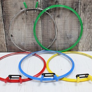 Könnte beinhalten: Fünf Stickrahmen in verschiedenen Farben: Rot, Blau, Gelb, Grün und Silber. Die Rahmen sind alle gleich groß und haben ein schlichtes Design.