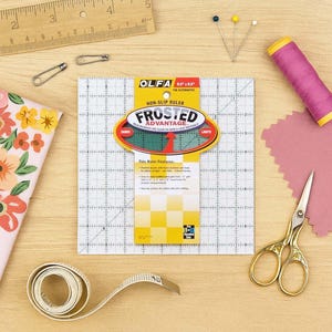 May include: A sewing and crafting scene with a non-slip ruler, measuring tape, pins, scissors, and thread. The ruler has a grid pattern and the text "FROSTED ADVANTAGE". A wooden ruler and floral fabric are also present.