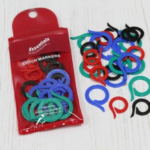 May include: A red pouch with the text "Essentials All your knitting needs" and "Stitch Markers" on the front. The pouch contains a variety of colorful plastic stitch markers in red, blue, green, and black.