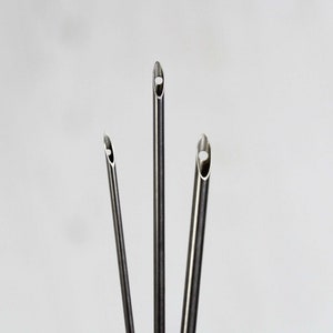 Könnte beinhalten: Drei silberne Metallröhren mit einer hohlen, abgerundeten Spitze. Die Röhren sind in Dreiecksform angeordnet.