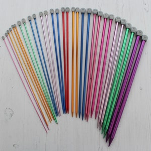 May include: A set of 20 colorful knitting needles with gray plastic tips. The needles are arranged in a fan shape on a white wooden surface. The needles are labeled with their sizes in millimeters.