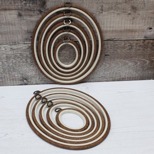 May include: Set of six oval embroidery hoops with wooden frames and white inner rings. The hoops are nested together in a decreasing size order.