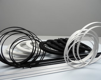 May include: A collection of black and white flexible plastic trim, arranged in a decorative pattern. The trim is in the shape of circles and is stacked on top of each other.