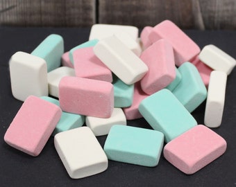 May include: A collection of rectangular erasers in various pastel colors, including pink, mint green, and white. The erasers are scattered, creating a visually appealing arrangement. The erasers are likely for school or office use.