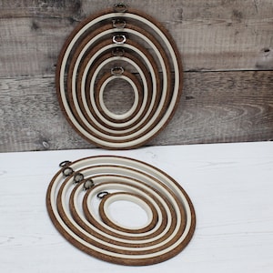 Peut inclure: Ensemble de six cerceaux de broderie ovales avec des cadres en bois et des anneaux intérieurs blancs. Les cerceaux sont imbriqués les uns dans les autres par ordre de taille décroissante.