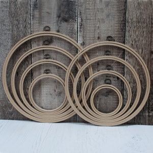 May include: A set of six wooden embroidery hoops of varying sizes, arranged in a circle on a wooden background. The hoops are made of natural wood and have a smooth finish.