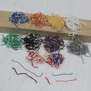 Könnte beinhalten: Eine Sammlung farbiger elastischer Kordeln mit weißen Kunststoffenden, angeordnet in Haufen und einzelnen Strängen. Farben sind Blau, Orange, Gelb, Weiß, Grün, Schwarz, Lila, Grau und Rot. Die Kordeln liegen auf einer Holzoberfläche.