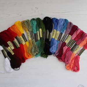 May include: A collection of 20 embroidery floss spools in various colors, including red, orange, yellow, green, blue, purple, and pink. Each spool has a black and gold label with the brand name "DMC" printed on it.