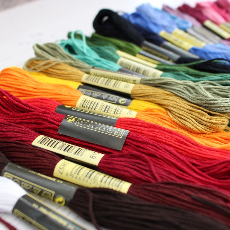 May include: A rainbow assortment of embroidery floss spools with black labels and white text. The labels include a barcode and washing instructions.