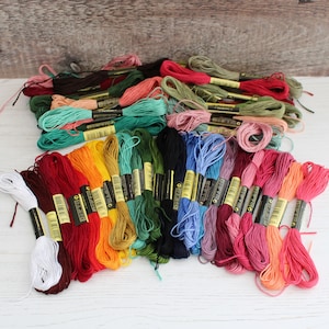 May include: A collection of embroidery floss spools in a variety of colors, including red, orange, yellow, green, blue, purple, pink, and brown. The spools are arranged in a rainbow pattern.