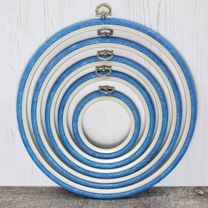 May include: Set of six blue and white embroidery hoops with silver metal rings. The hoops are nested inside each other, with the largest hoop on the outside and the smallest hoop on the inside.