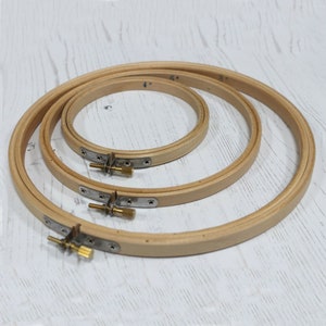 May include: Three wooden embroidery hoops, 4 inches, 6 inches, and 8 inches in diameter. The hoops are nested inside each other, with the largest hoop on the bottom and the smallest hoop on top.