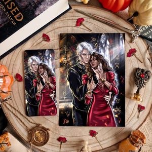 May include: A book, bookmark, and art print featuring a couple in a romantic embrace. The woman wears a red dress, and the man is in a black jacket. The items are arranged on a wooden surface with decorative elements.