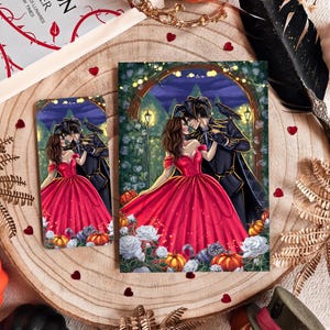May include: Two art prints depicting a romantic illustration of a couple in formal attire, surrounded by pumpkins and flowers. The woman wears a red gown. A book, a crown, and a decorative pumpkin are also visible.