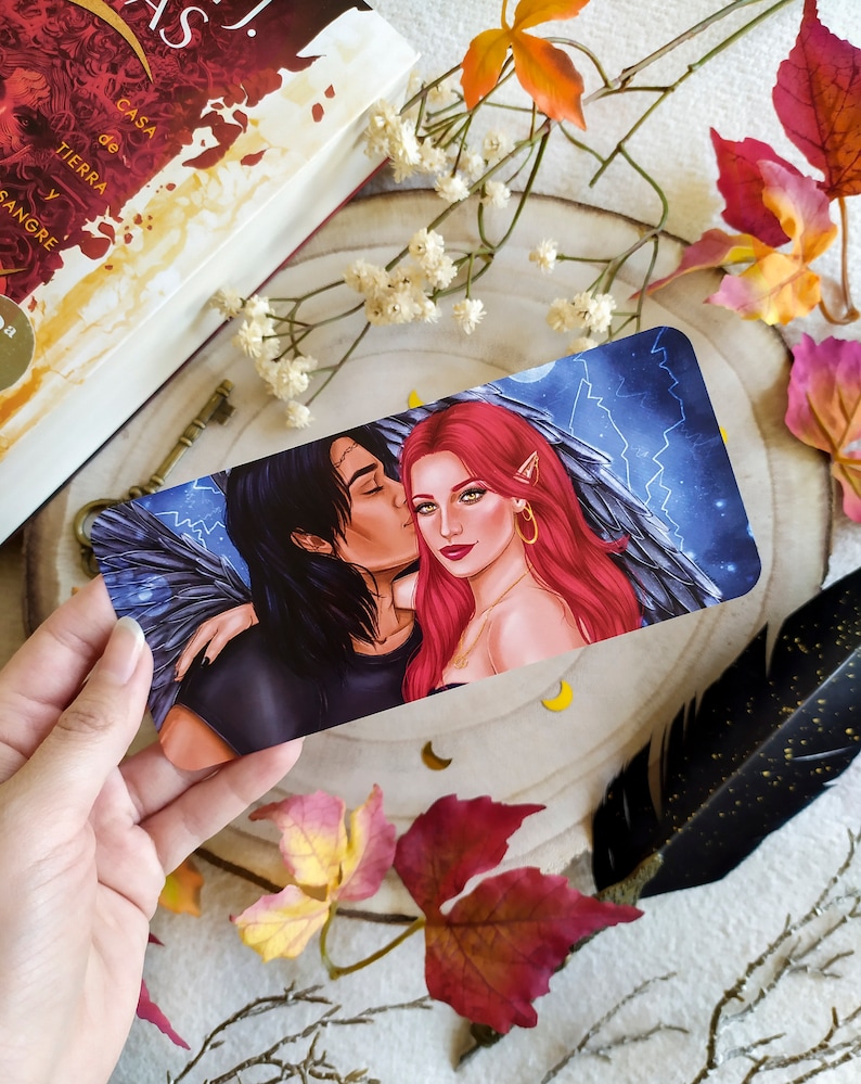 Puede incluir: Un marcap&aacute;ginas con una pareja con alas, la mujer tiene el pelo rojo y lleva un collar de oro, el hombre tiene el pelo oscuro y lleva una camisa negra. El fondo es un cielo azul con rayos.