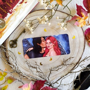 Puede incluir: Una tarjeta con una pareja en ella. El hombre tiene el pelo oscuro y lleva una camisa negra. La mujer tiene el pelo largo y rojo y lleva un vestido negro. El fondo es azul oscuro con rayos.