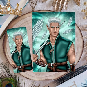 Puede incluir: Un marcapáginas y una impresión con un personaje de fantasía con cabello blanco, ojos verdes y una espada. El personaje lleva un atuendo verde y marrón con un ala blanca con plumas detrás. El fondo es un patrón verde y azul en espiral.