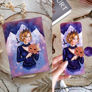 May include: A watercolor illustration of a woman with a crown, holding a mask in front of a mountain range. The woman is wearing a dark blue outfit with a black choker and a sword is behind her. The background is a purple and pink gradient with stars.