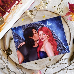 Puede incluir: Una impresi&oacute;n de una pareja abraz&aacute;ndose, la mujer tiene el pelo rojo y lleva un vestido negro, el hombre tiene el pelo negro y lleva una camisa negra, est&aacute;n frente a un fondo azul oscuro con estrellas y una luna creciente.