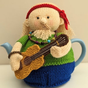 May include: A knitted teapot cosy in the shape of a person playing a guitar. The person has a long beard, a red headband, and is wearing a green shirt and blue trousers.