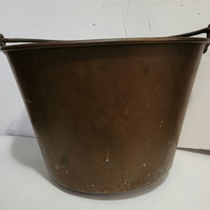 May include: A large, copper bucket with a metal handle. The bucket has a worn, aged appearance with a patina finish.