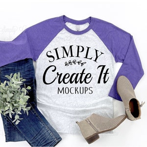 May include: A mock-up image featuring a gray and purple raglan-style long-sleeve shirt with the text "SIMPLY Create It MOCKUPS" in black. The shirt is paired with blue jeans, a pair of tan ankle boots, and a small green plant on a white background.