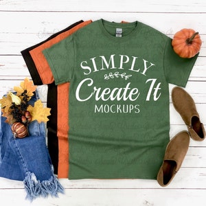 Op de afbeelding: Een stapel van drie T-shirts met korte mouwen in olijfgroen, oranje en zwart. Het bovenste olijfgroene shirt heeft witte tekst met de tekst SIMPLY Create It MOCKUPS en een kleine bladgrafiek. Het geheel is gecombineerd met een blauwe spijkerbroek, een kleine pompoen en bruine laarzen.
