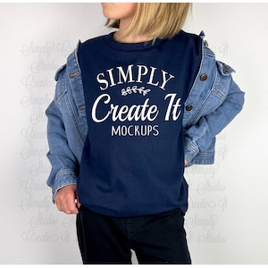 Könnte beinhalten: Ein marineblaues T-Shirt mit dem Text "SIMPLY Create It MOCKUPS" in Weiß. Das Shirt wird von einer Person getragen, die eine Jeansjacke und eine schwarze Hose trägt.